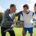 Mature coach teaching strategy to high school team on football field. Young soccer players standing together united and listening coach motivational speech. Coach giving team advise before school match.