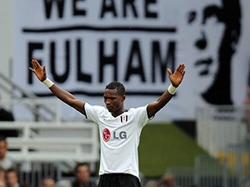 John Pantsil prays with his arms out-stretched in front of a giant "We Are Fulham" banner