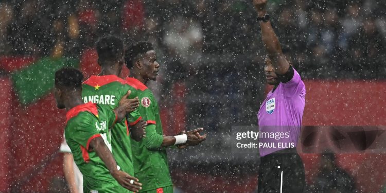 Ghanaian referee Daniel Nii Ayi Laryea (R) gives a yellow card to Burkina Faso's midfielder #20 Gustavo Sangare during the Africa Cup of Nations (CAN) Group E football match between Algeria and Burkino Faso at Moulay Hassan Stadium in Rabat on December 28, 2025. (Photo by Paul ELLIS / AFP via Getty Images)