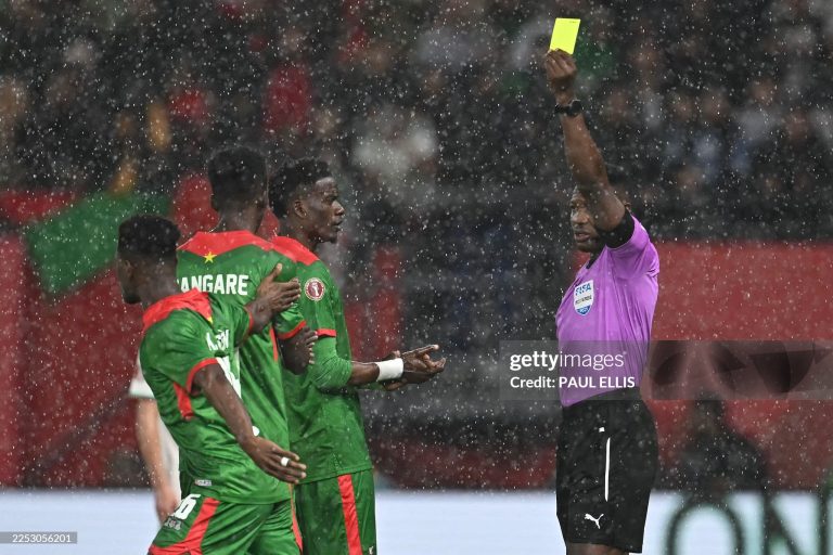 Ghanaian referee Daniel Nii Ayi Laryea (R) gives a yellow card to Burkina Faso's midfielder #20 Gustavo Sangare during the Africa Cup of Nations (CAN) Group E football match between Algeria and Burkino Faso at Moulay Hassan Stadium in Rabat on December 28, 2025. (Photo by Paul ELLIS / AFP via Getty Images)